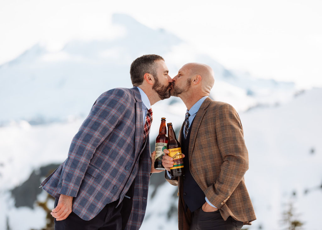 Two grooms kissing with beer on their elopement day